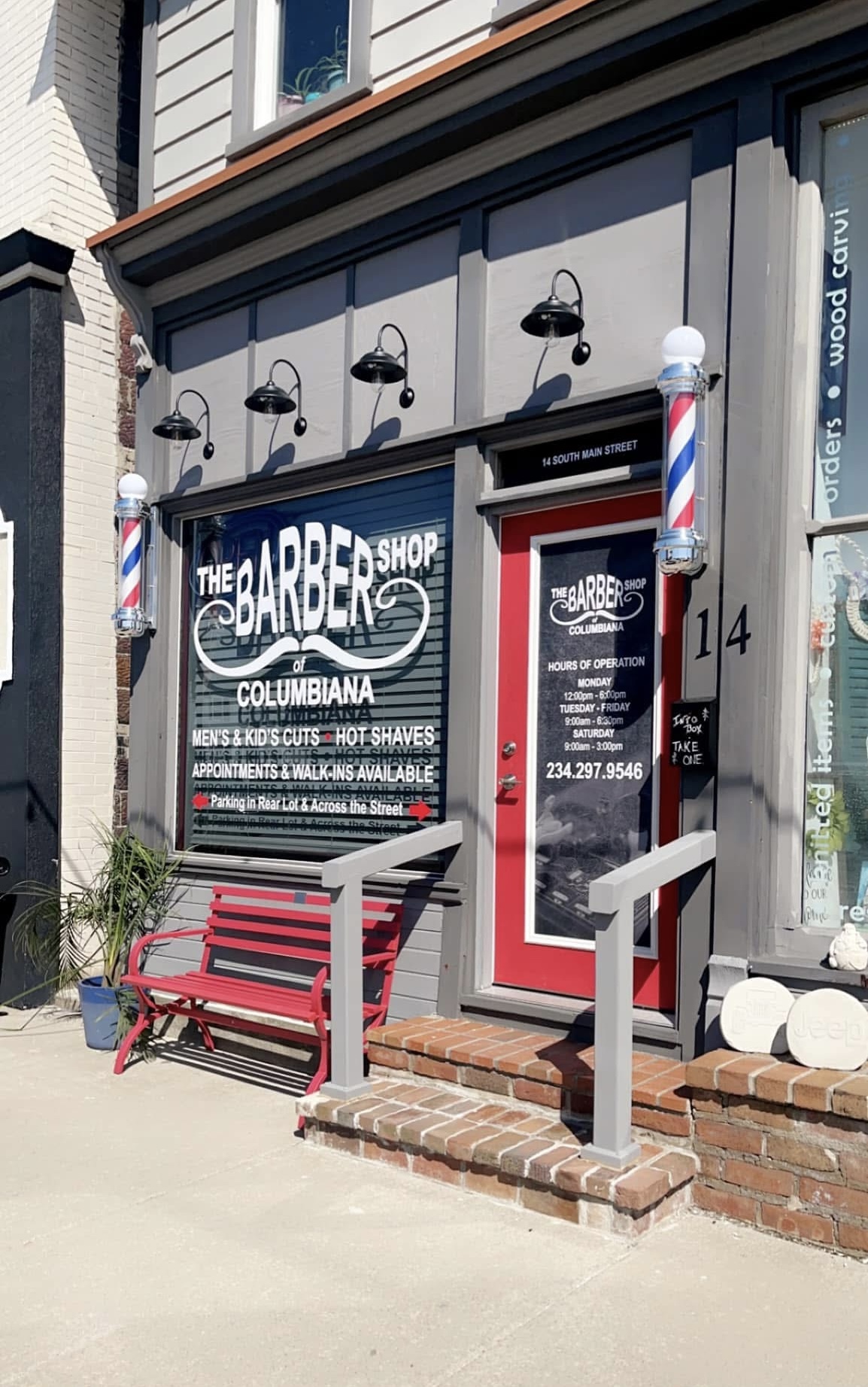 The Barbershop of Columbiana storefront with its red door and barber poles
